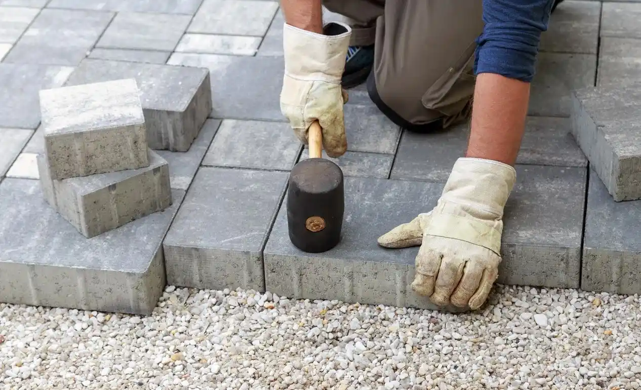 a person with gloves holding a mallet and a hammer while doing Paver Installation in Dallas